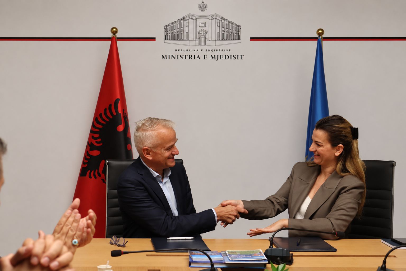 Signature d’une convention de partenariat entre les Explorations de Monaco et l’Albanie, avec une poignée de main entre les représentants devant les drapeaux albanais et européen.